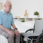 old man sitting on the bed with wheelchair near